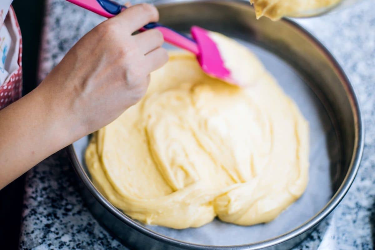 Adding cake batter to a cake pan.