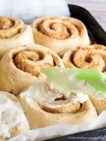 A photo of spreading the icing over the cinnamon rolls.