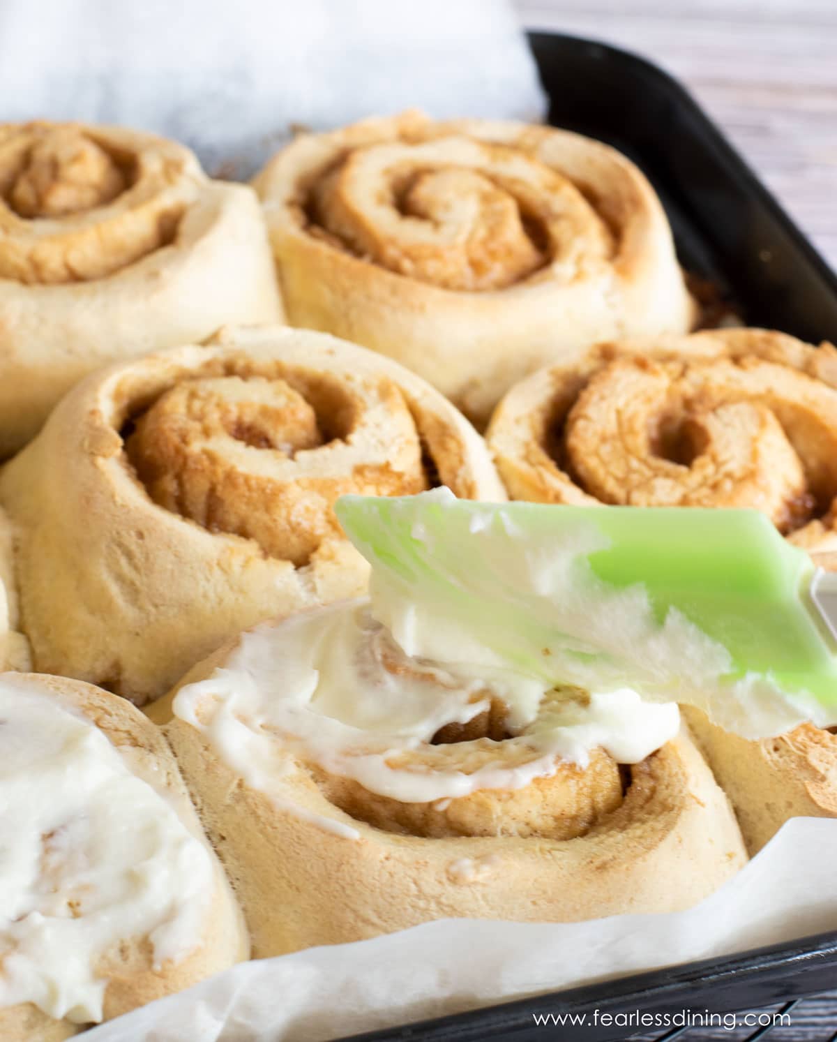 A photo of spreading the icing over the cinnamon rolls.