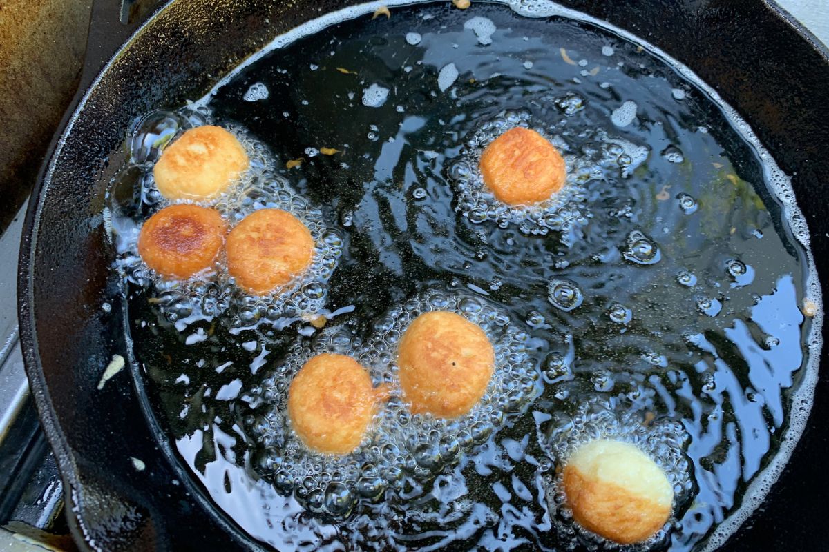 Donut holes frying in oil in a cast iron skillet.