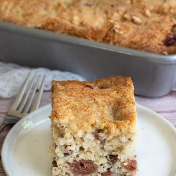 A slice of gluten free cherry cake on a plate next to the cake.