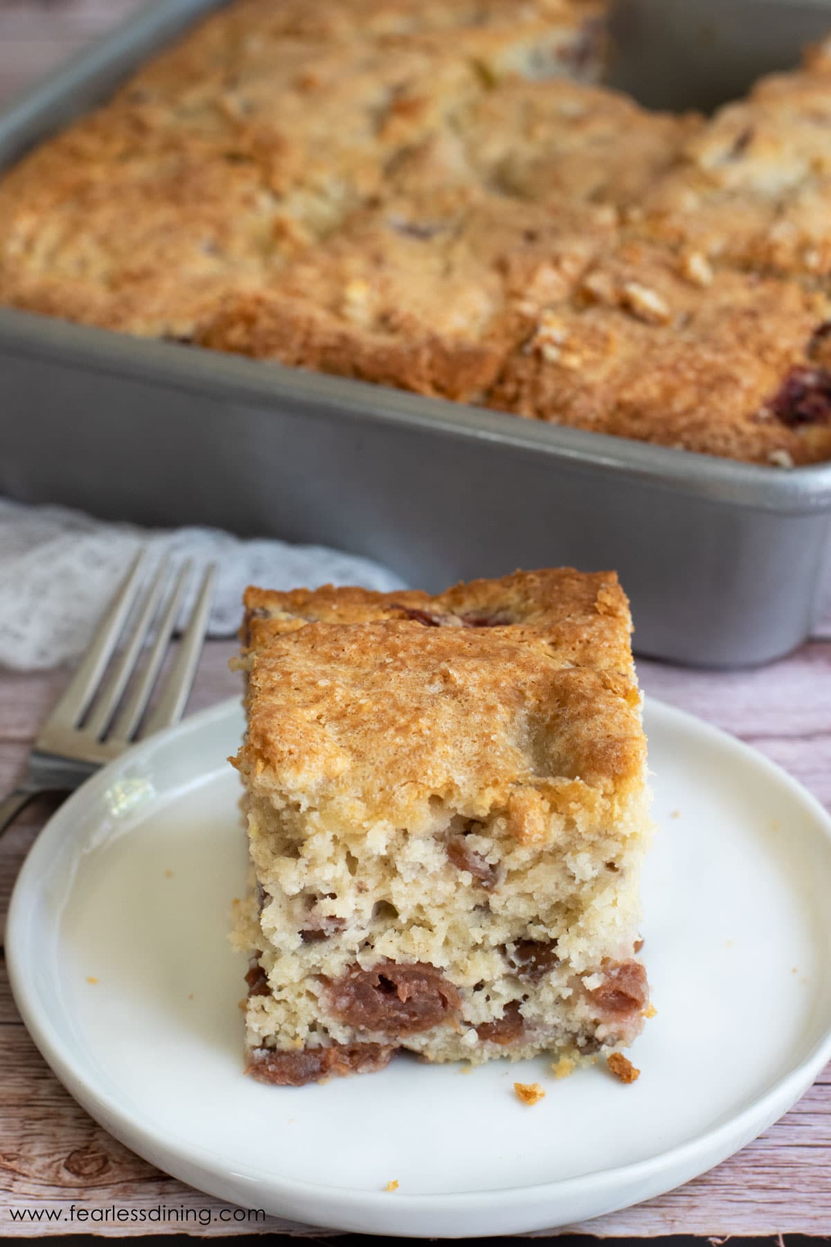 A slice of gluten free cherry cake on a plate next to the cake.