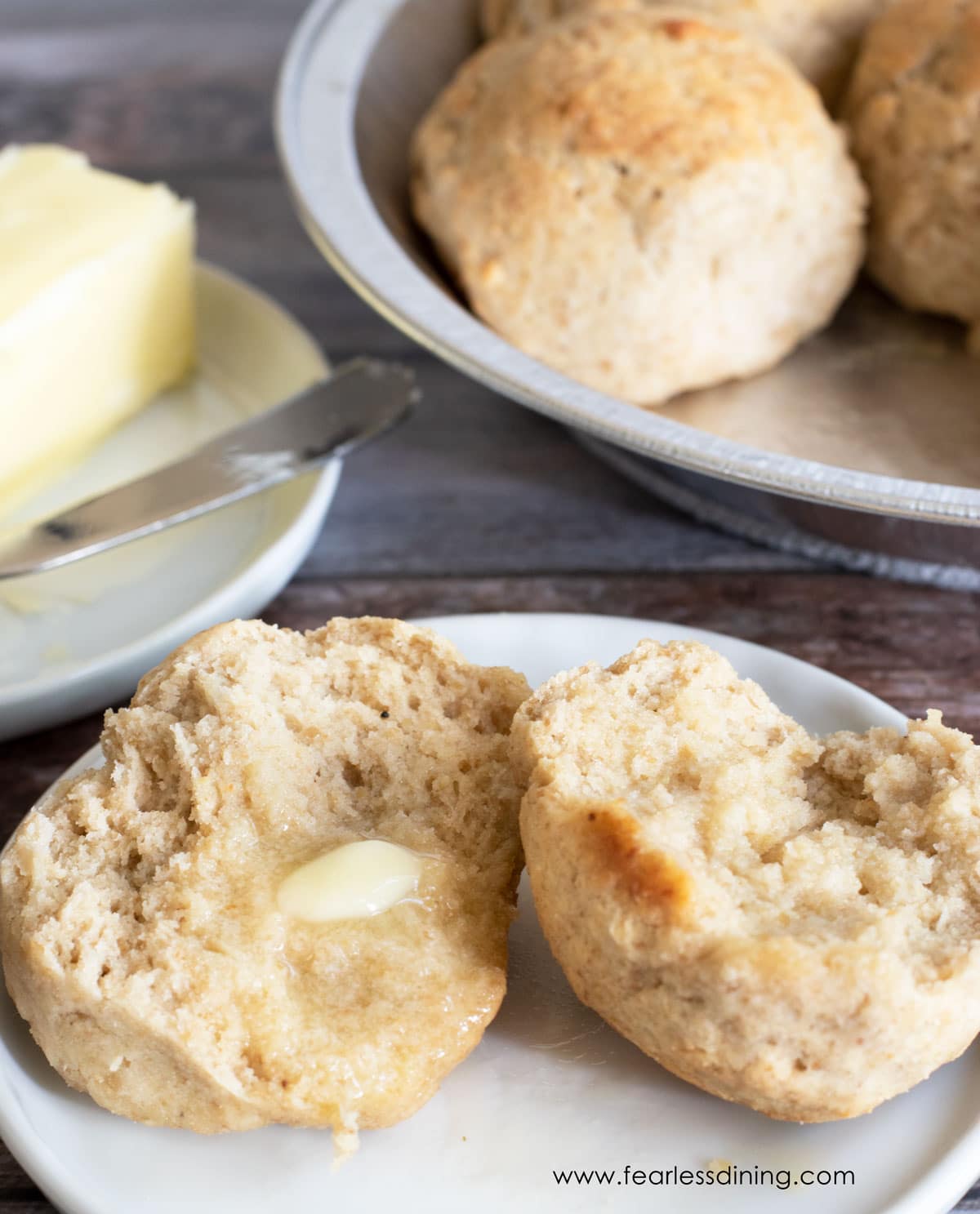 A gluten free yeast roll cut on a plate with melted butter spread onto each half.