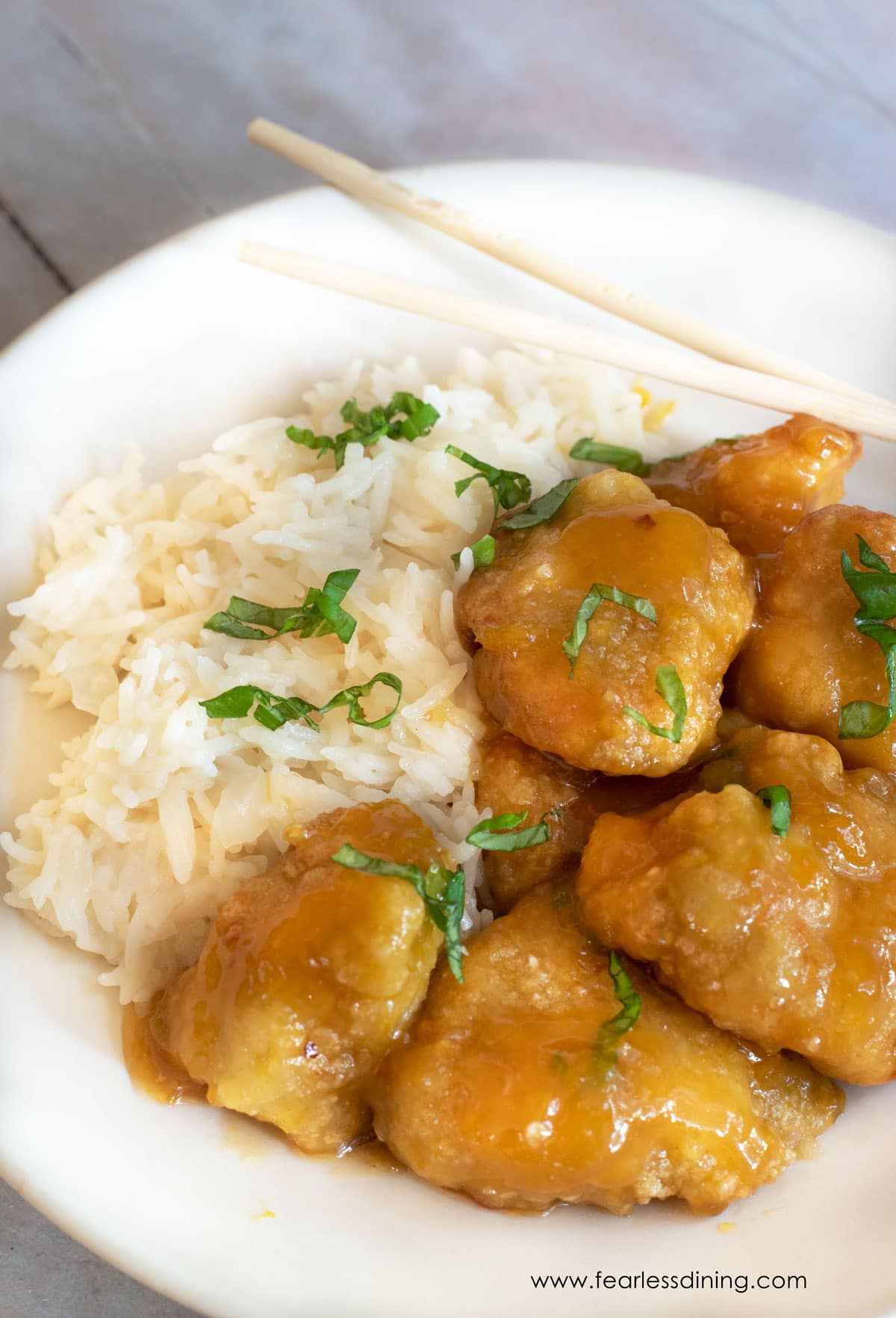 A big white dinner plate with orange chicken over rice.