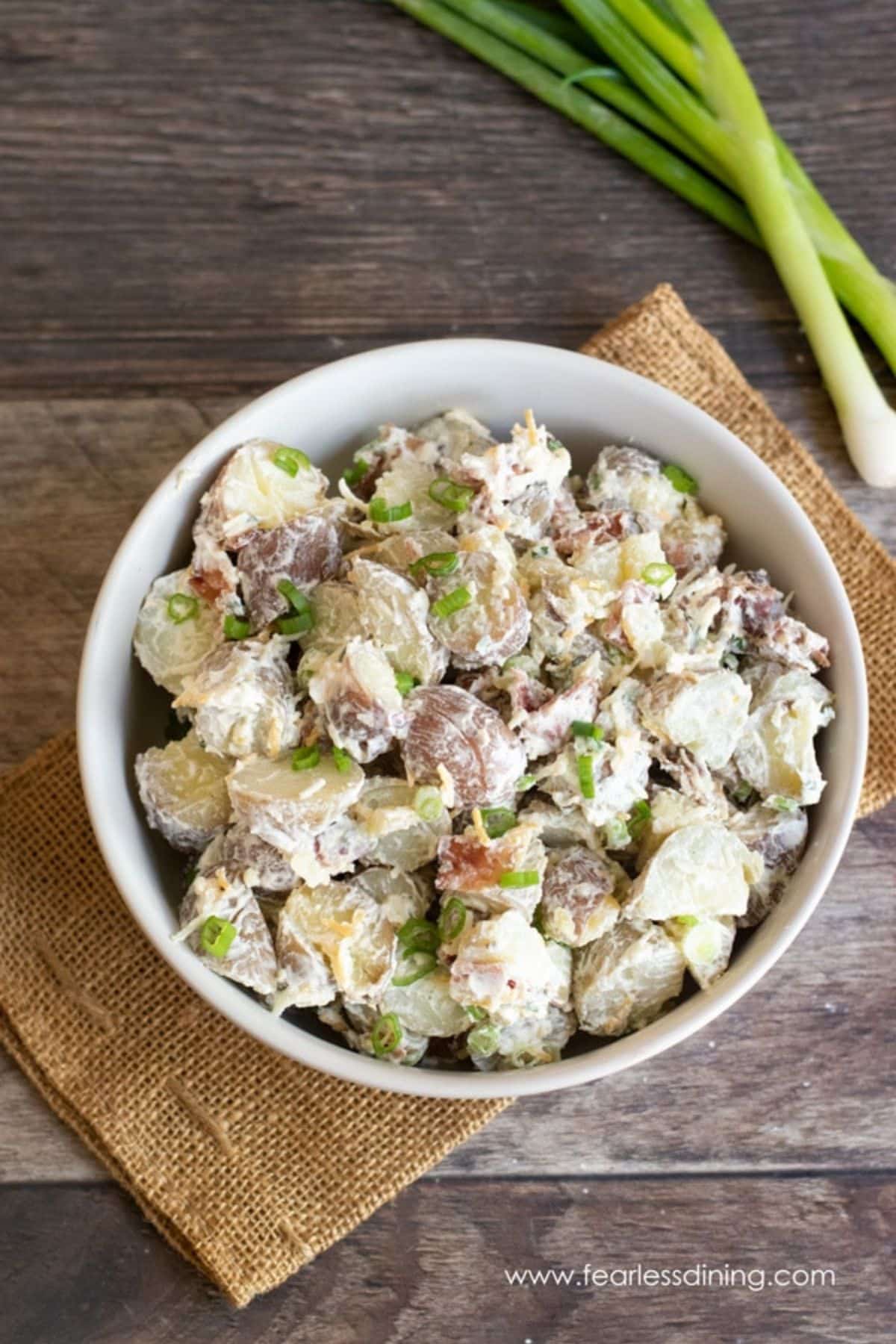 A bowl of loaded potato salad on a wooden table.