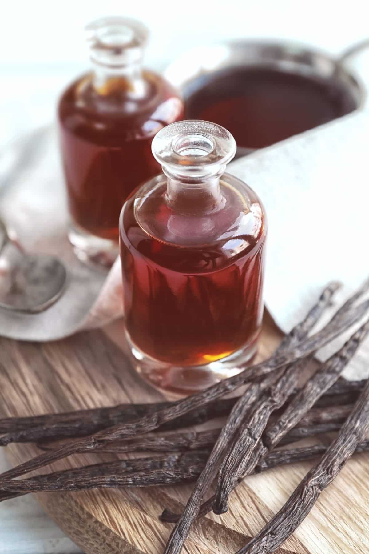 Two glass jars of vanilla extract on a cutting board.