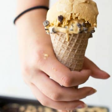 A hand holding an ice cream cone with caramel chip ice cream.