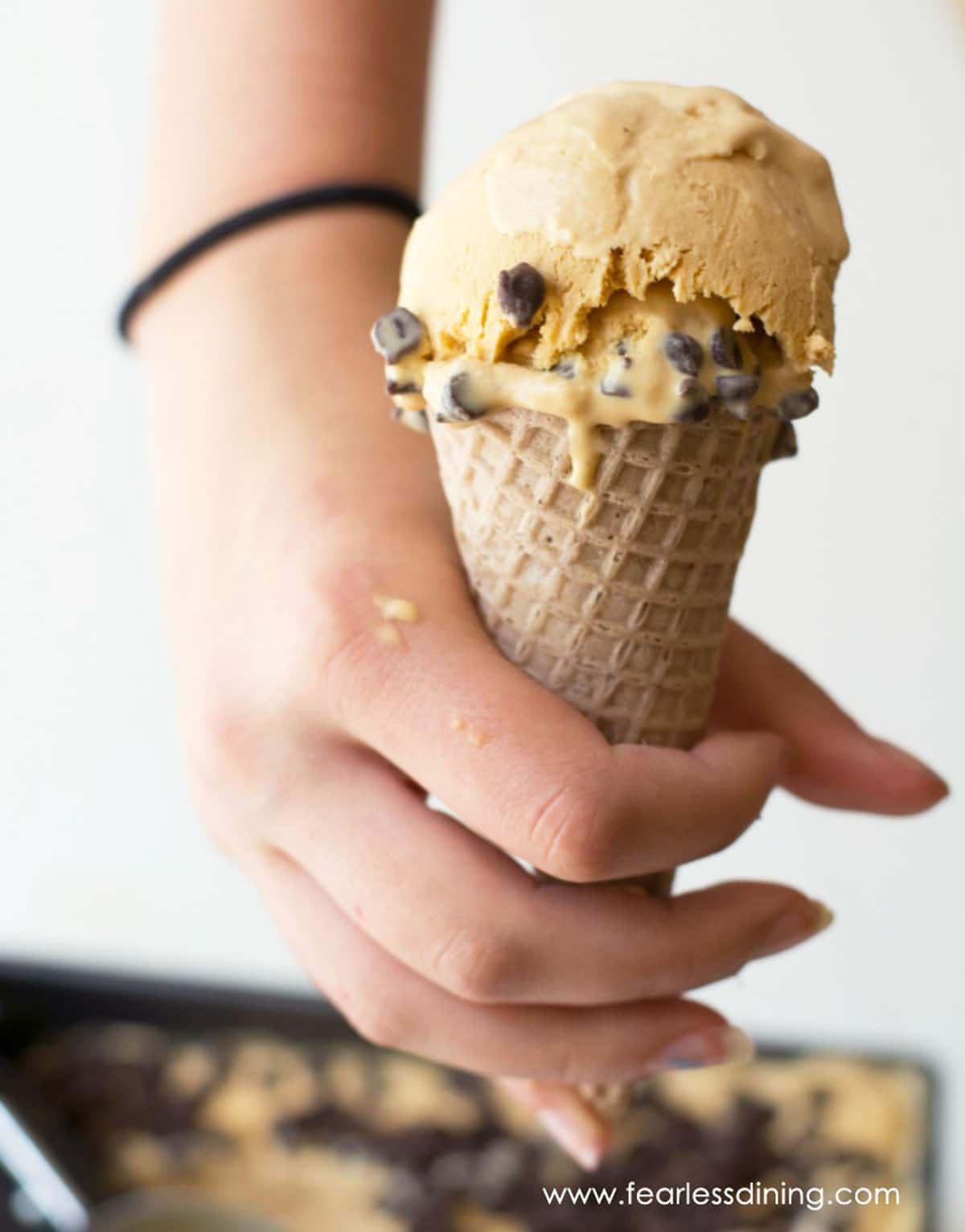 A hand holding an ice cream cone with caramel chip ice cream.