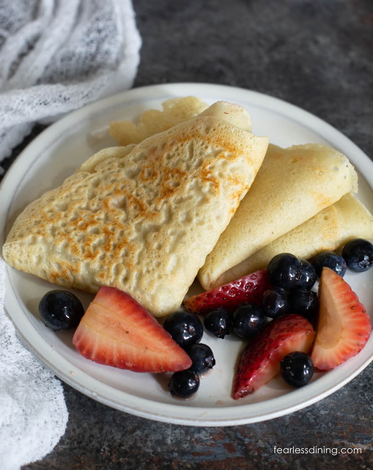 Folded crepes on a plate with fresh berries.