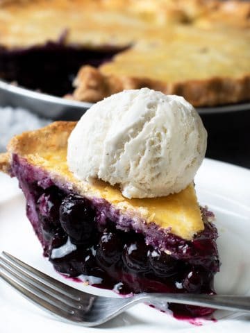 a slice of blueberry pie topped with a scoop of vanilla ice cream.