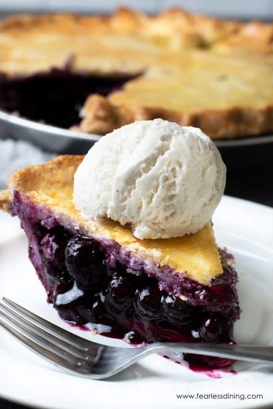 A slice of blueberry pie topped with a scoop of vanilla ice cream.