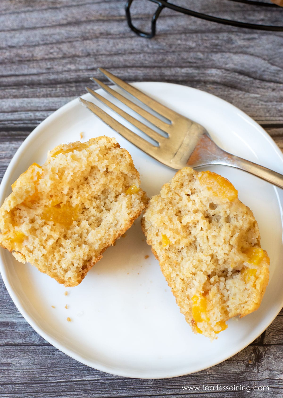A gluten free peach muffin cut in half on a plate so you can see the peach chunks inside.
