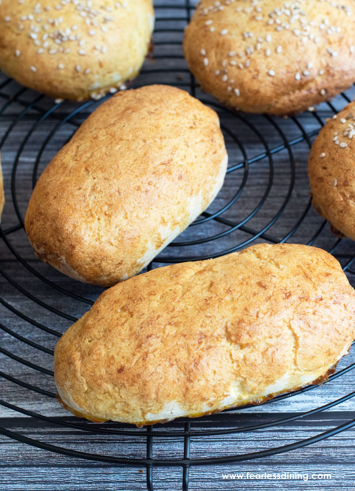 Some baked hot dog buns cooling on a rack.