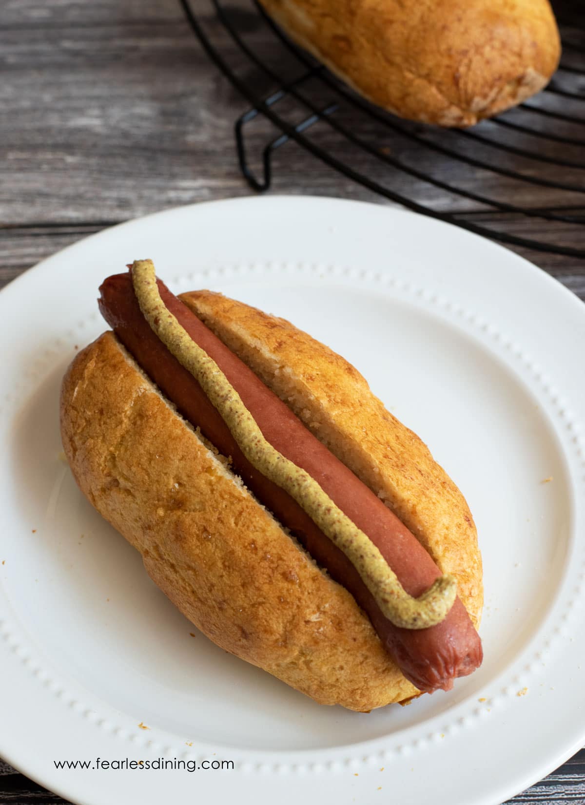 A hot dog in a gluten free hot dog bun on a white plate.