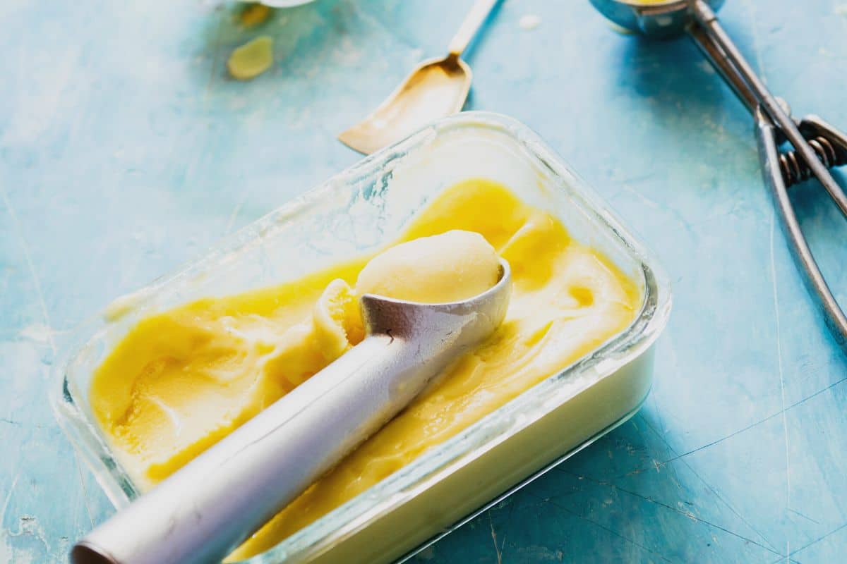 Frozen pineapple sorbet in a container. There is an ice cream scoop in the sorbet.