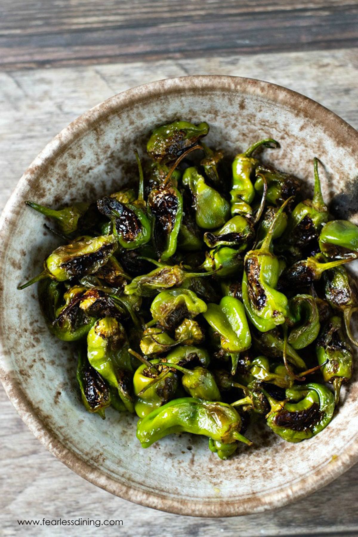 A pottery bowl filled with roasted padron peppers.