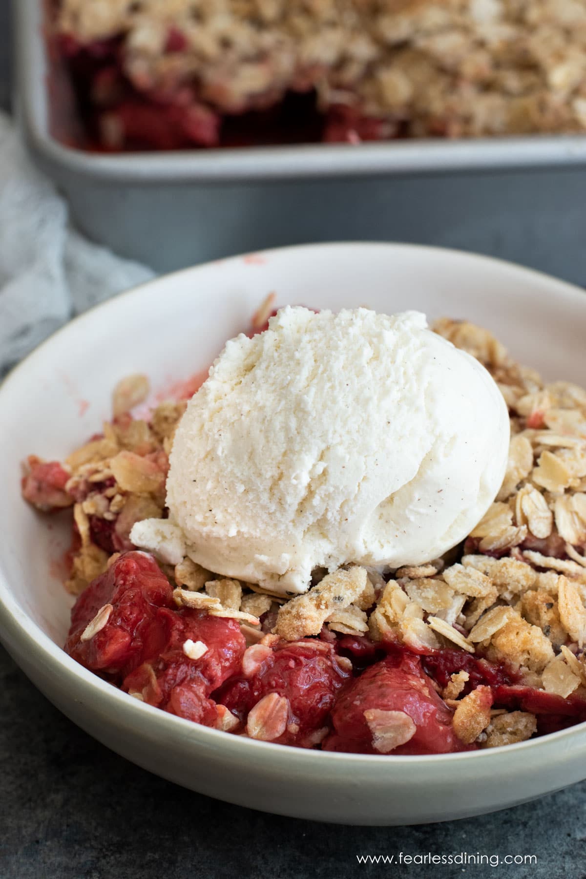 A bowl of gluten free strawberry rhubarb crisp with a scoop of vanilla ice cream.