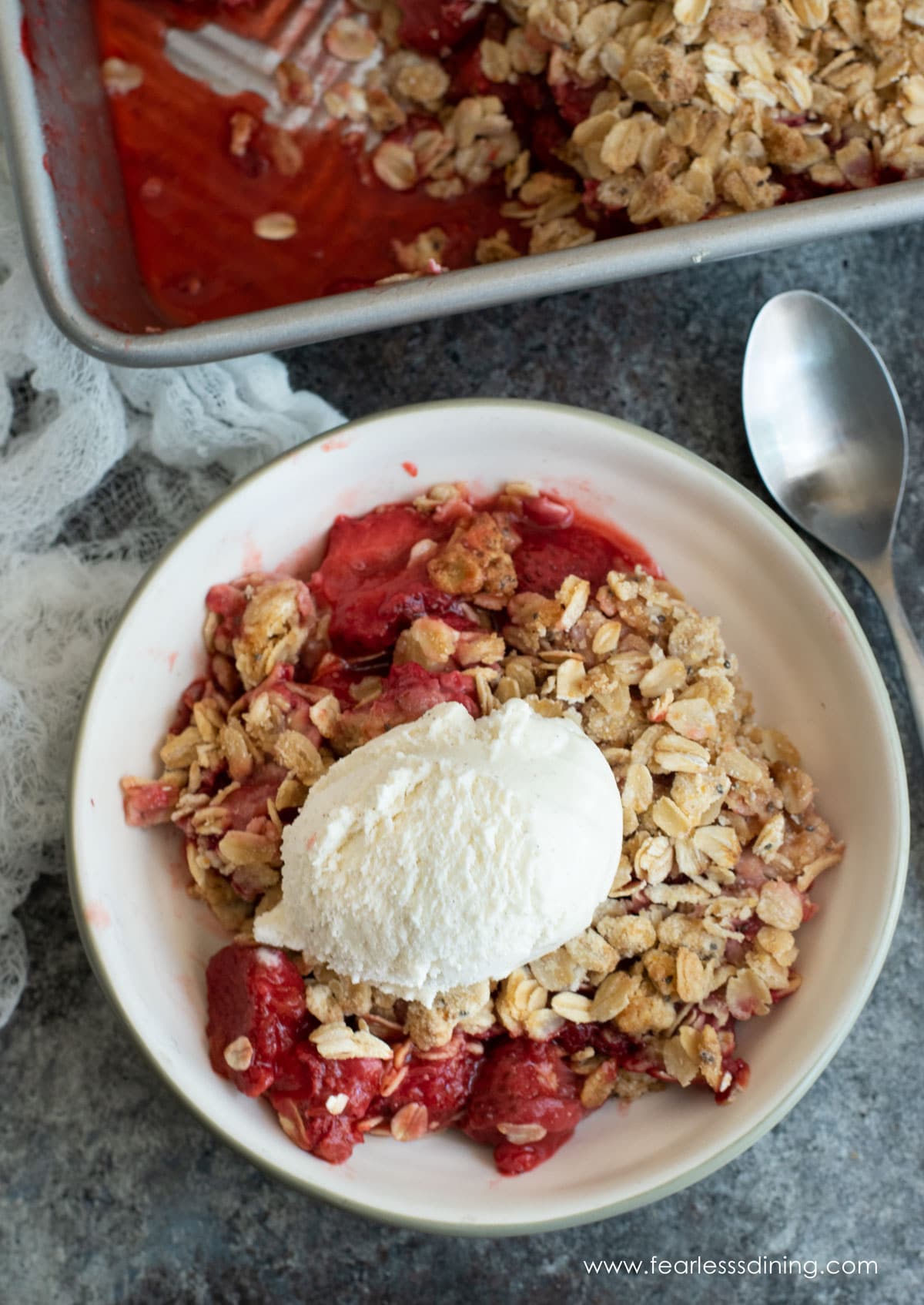 The top view of a bowl of gluten free strawberry rhubarb crisp with vanilla ice cream.