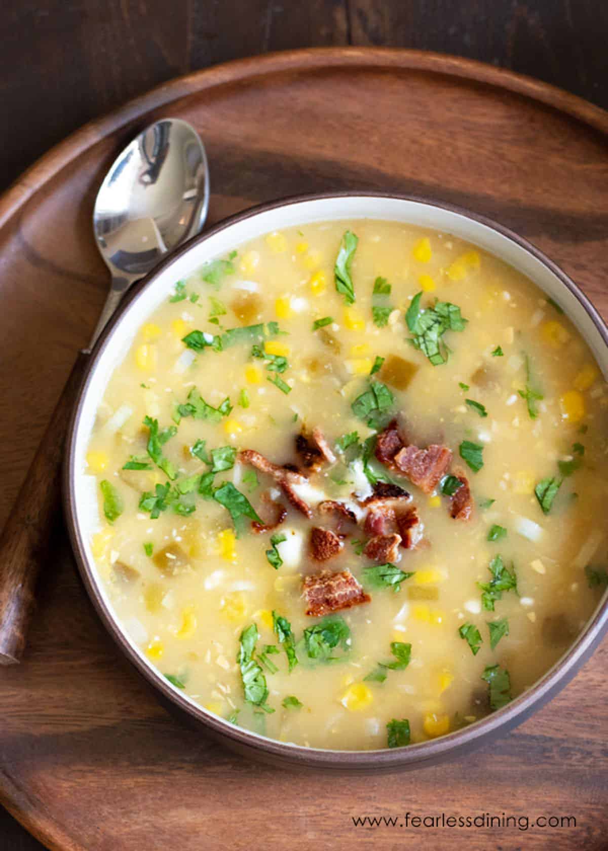 A bowl of gluten free corn chowder on a wooden serving platter.