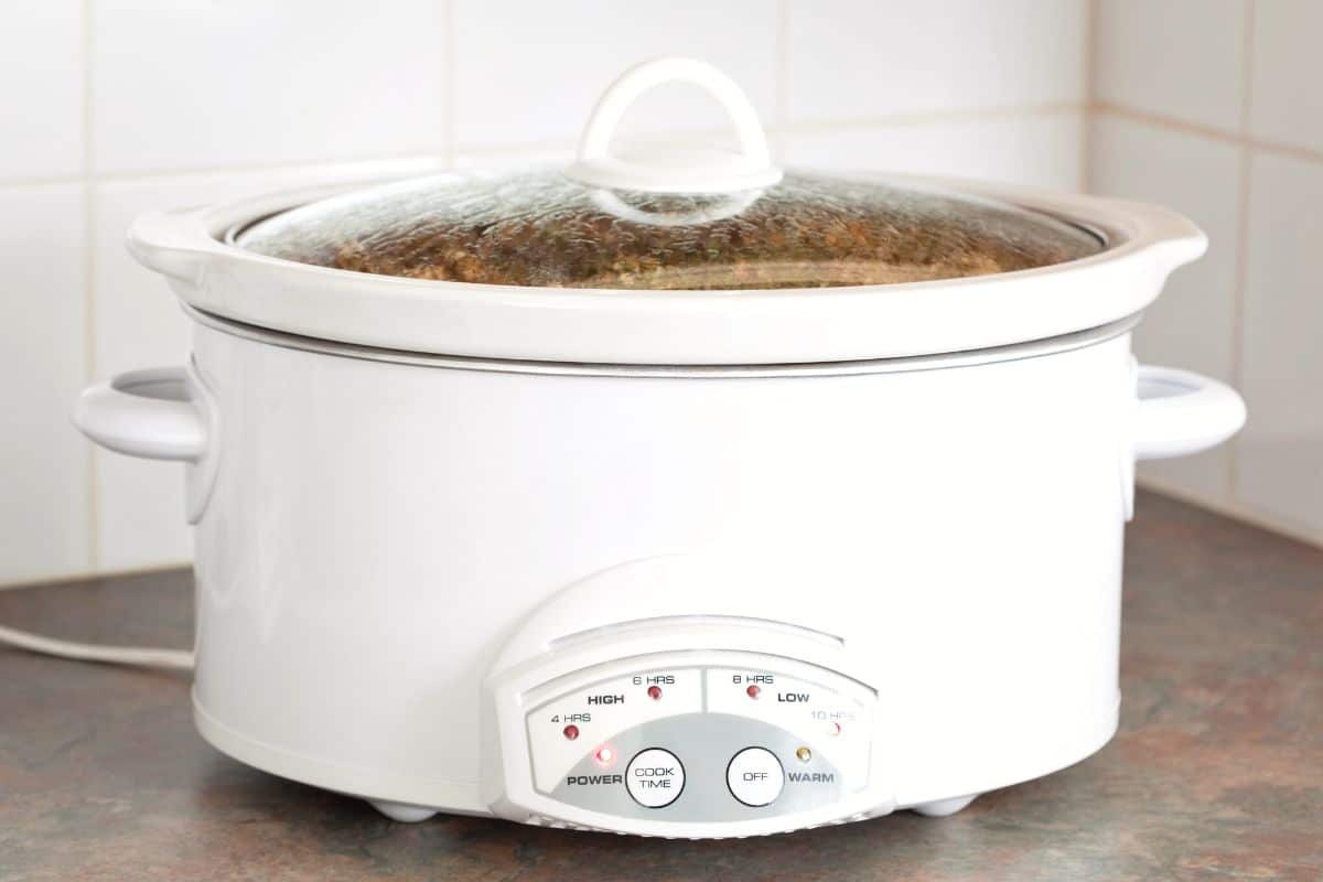 Pulled pork cooking in a white slow cooker.