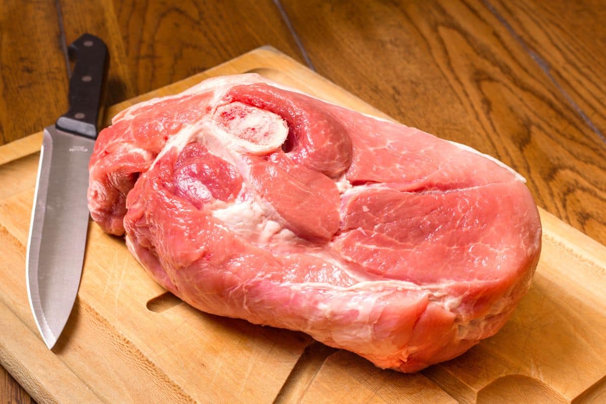 raw pork shoulder on a cutting board with a knife.