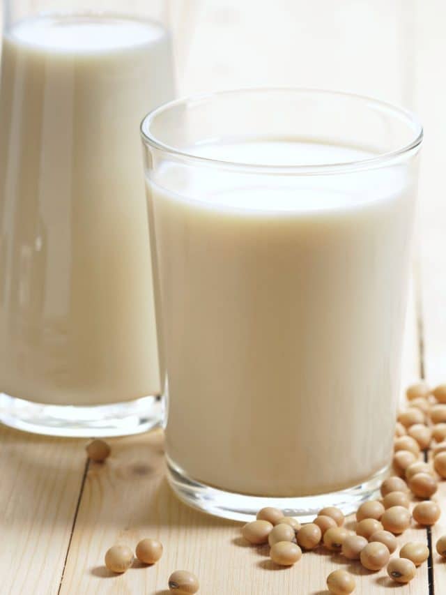 A glass of soy milk next to a carafe of soy milk on a table.