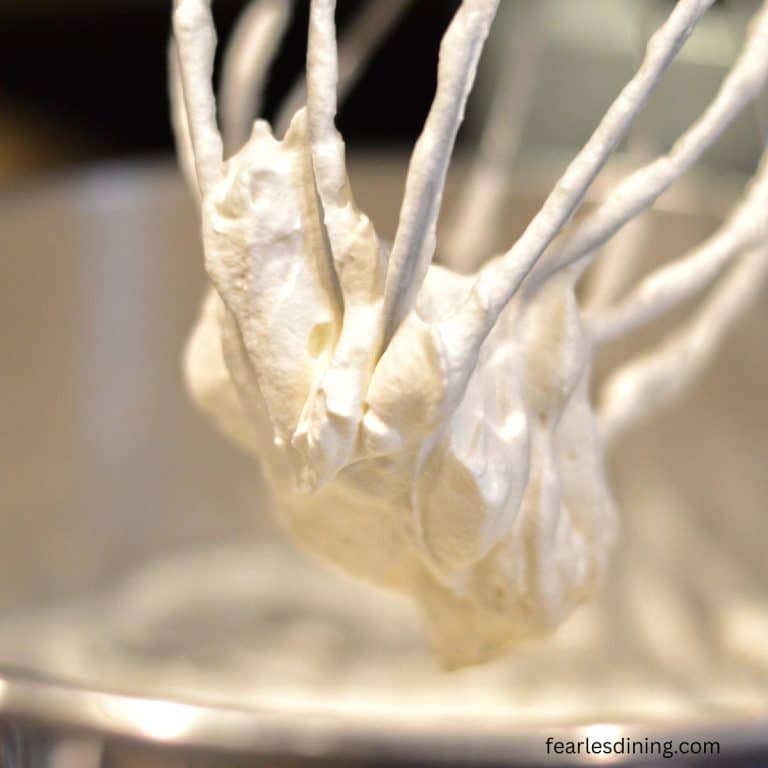 A mixer whisk attachment with whipped heavy cream on it.