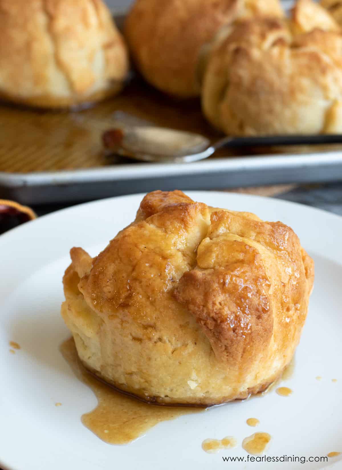 A baked gluten free apple dumpling on a plate with the brown sugar sauce.