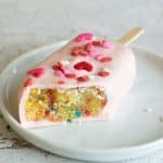 A funfetti cakesicle with a bite removed so you can see the funfetti cake inside.
