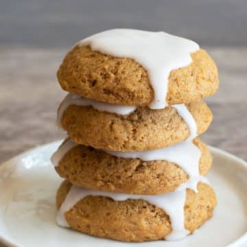 A stack of four iced pumpkin cookies on a plate.