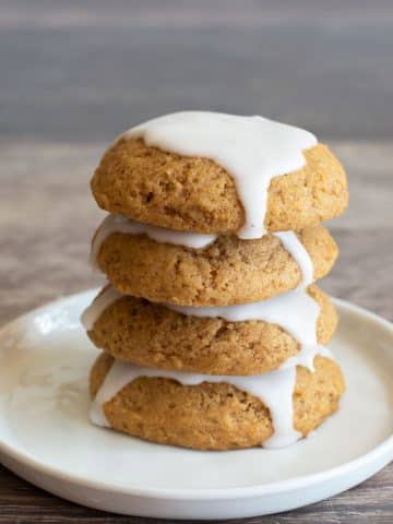 A stack of four iced pumpkin cookies on a plate.