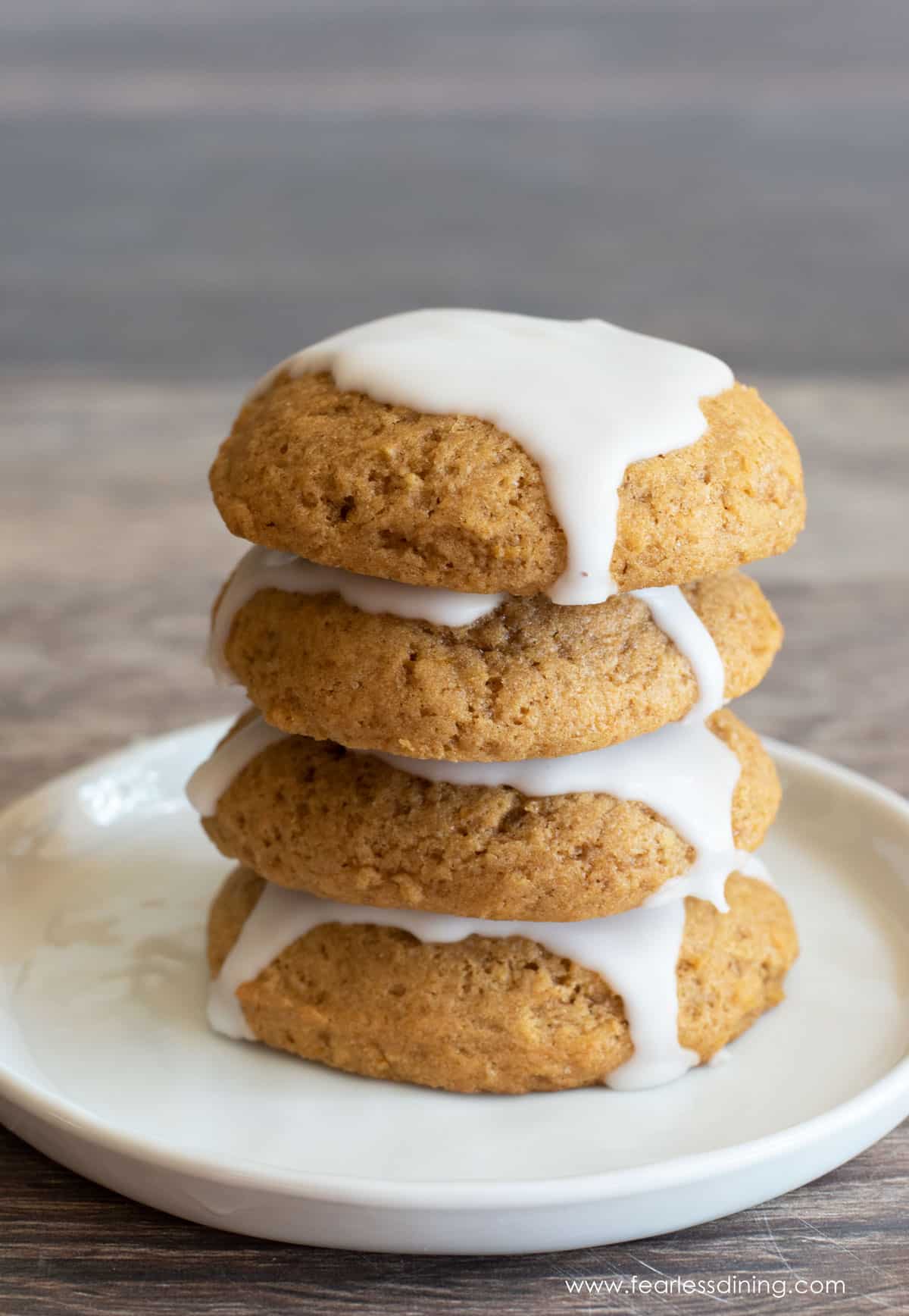 A stack of four iced pumpkin cookies on a plate.