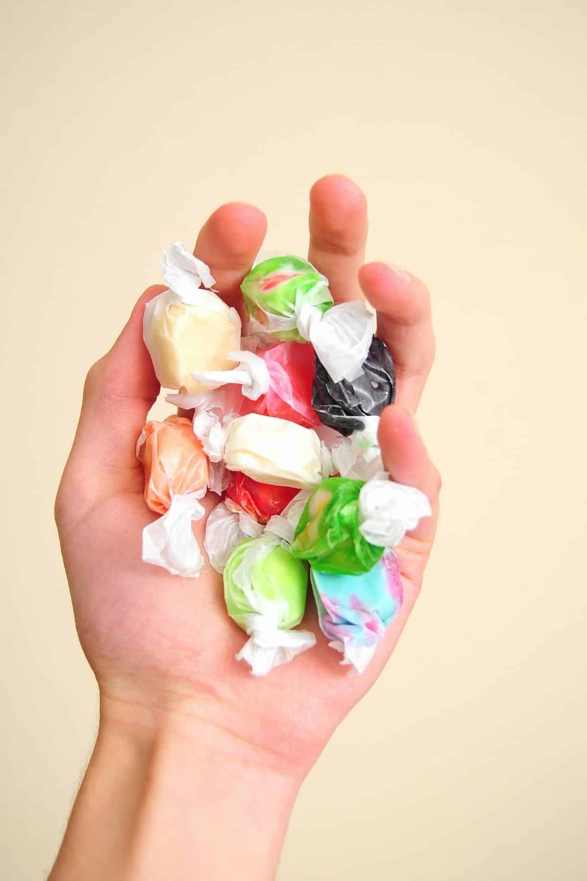 A hand holding wrapped salt water taffy pieces.