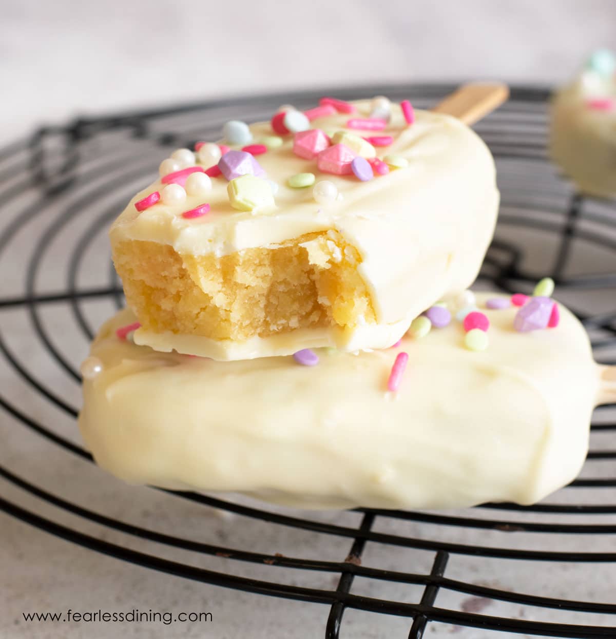 A white chocolate covered cakesicle with a bite taken out.