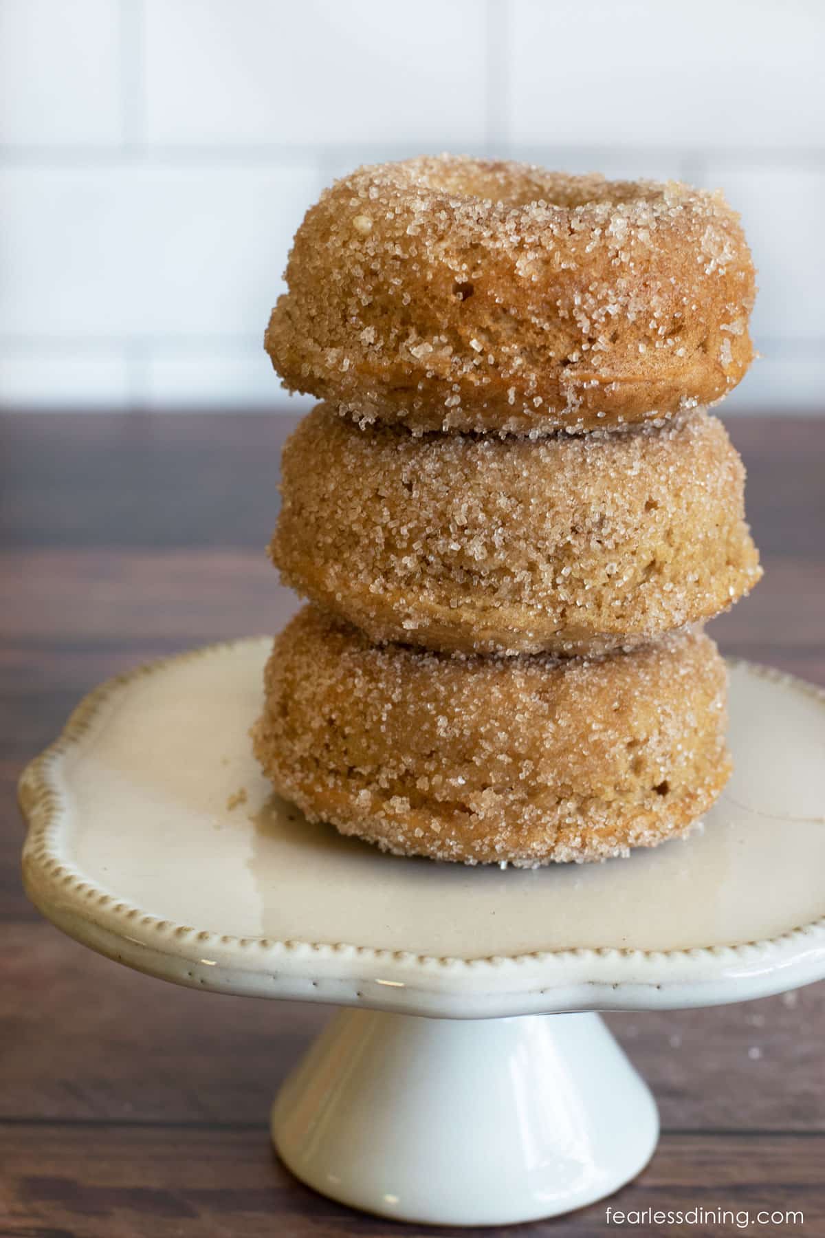 A stack of three gluten free apple cider donuts on a small pedestal.