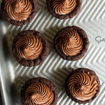 A baking tray with six chocolate cookie cups with chocolate frosting.