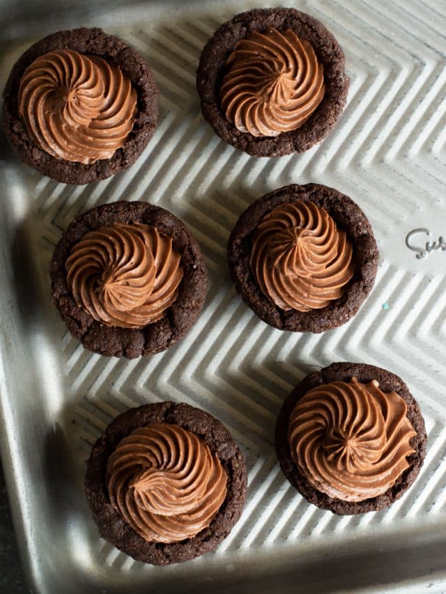 A baking tray with six chocolate cookie cups with chocolate frosting.