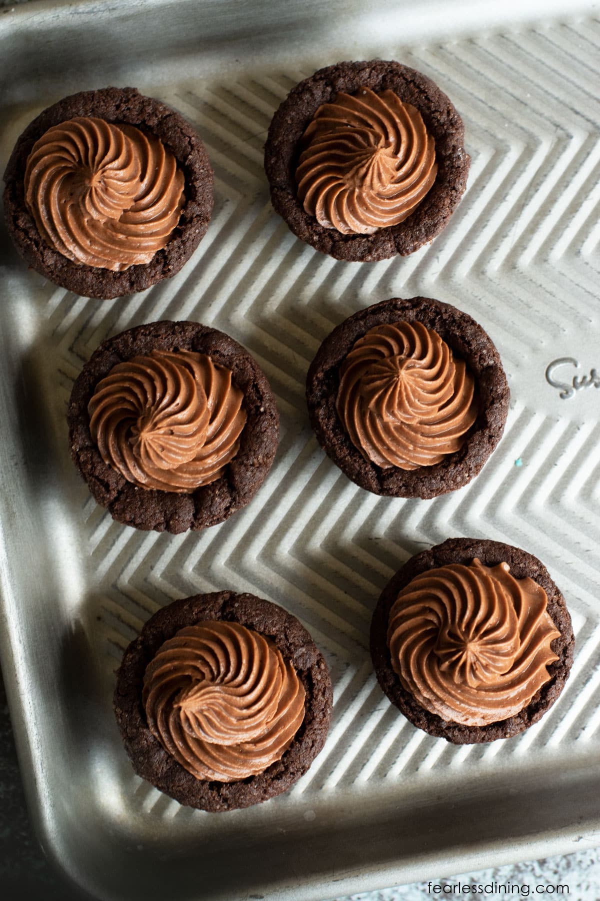 A baking tray with six chocolate cookie cups with chocolate frosting.