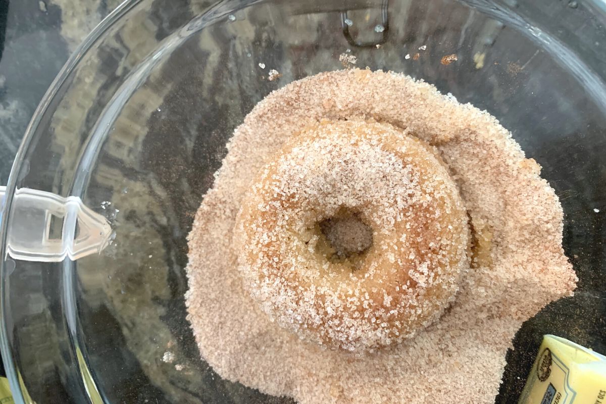 Dipping a donut in the cinnamon sugar.