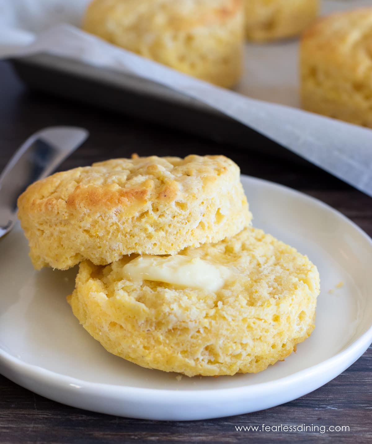 A cut biscuit on a white plate. The biscuit has a pad of butter melting on the bottom half.