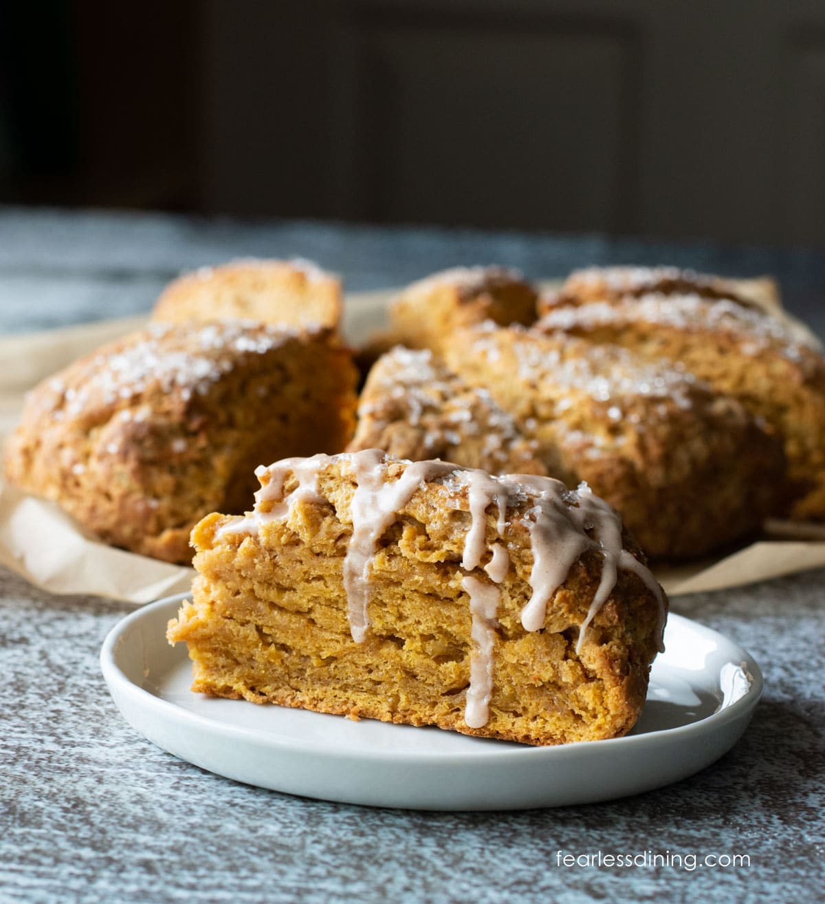 A photo of a pumpkin scone on a small white plate. Icing is dripping down the scone.