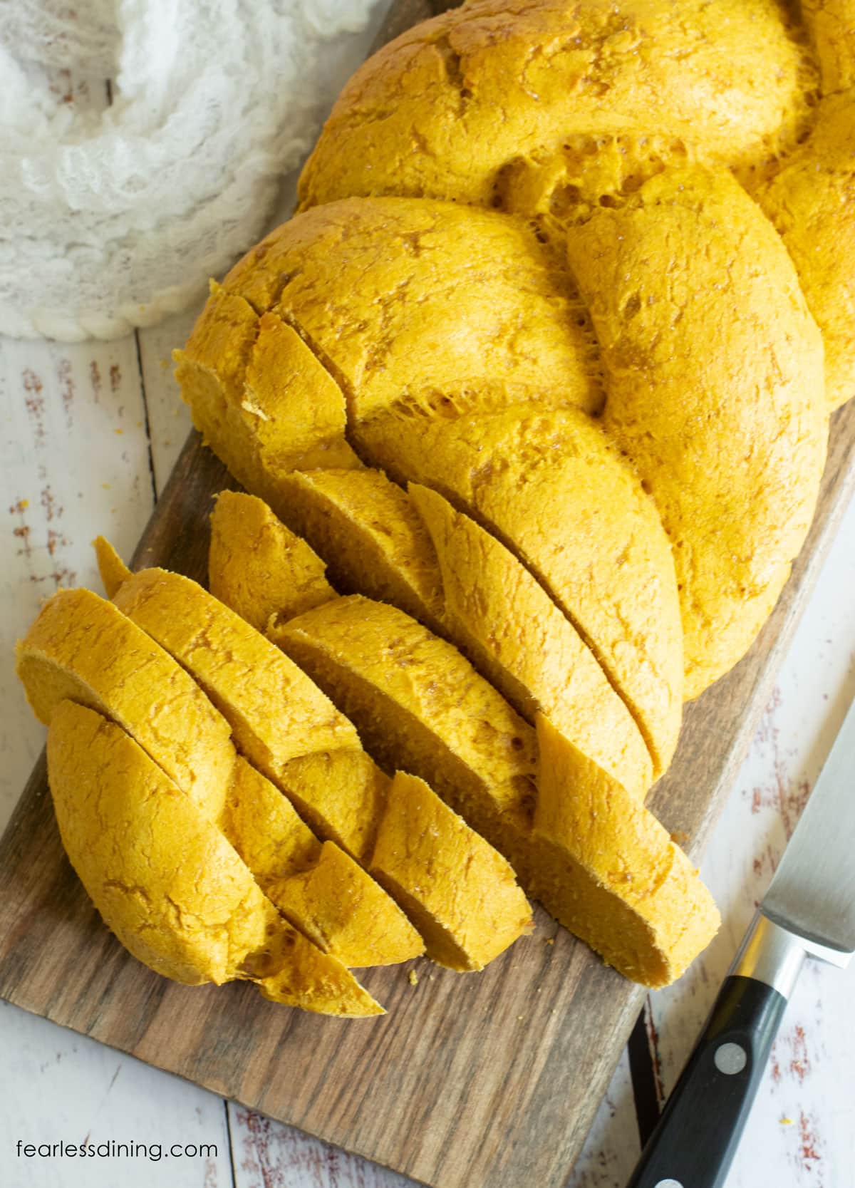 A pumpkin challah partially cut into slices on a cutting board.