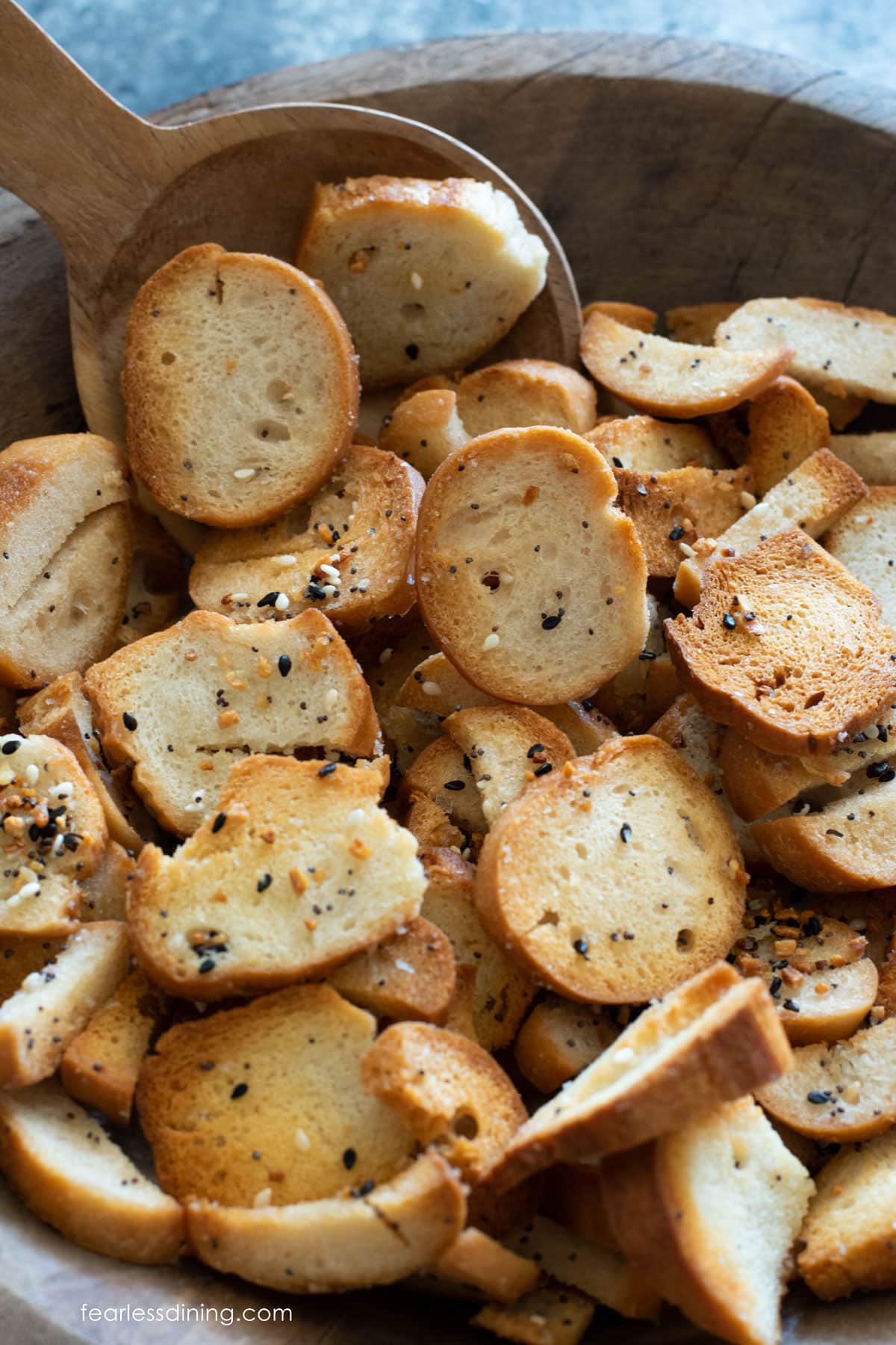 A wooden serving bowl full of bagel chips.