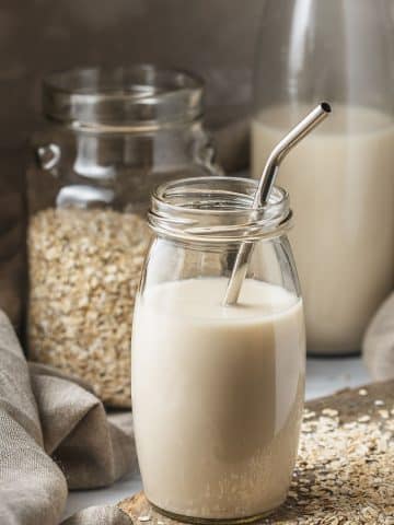 a glass of oat milk next to a jar of oats.