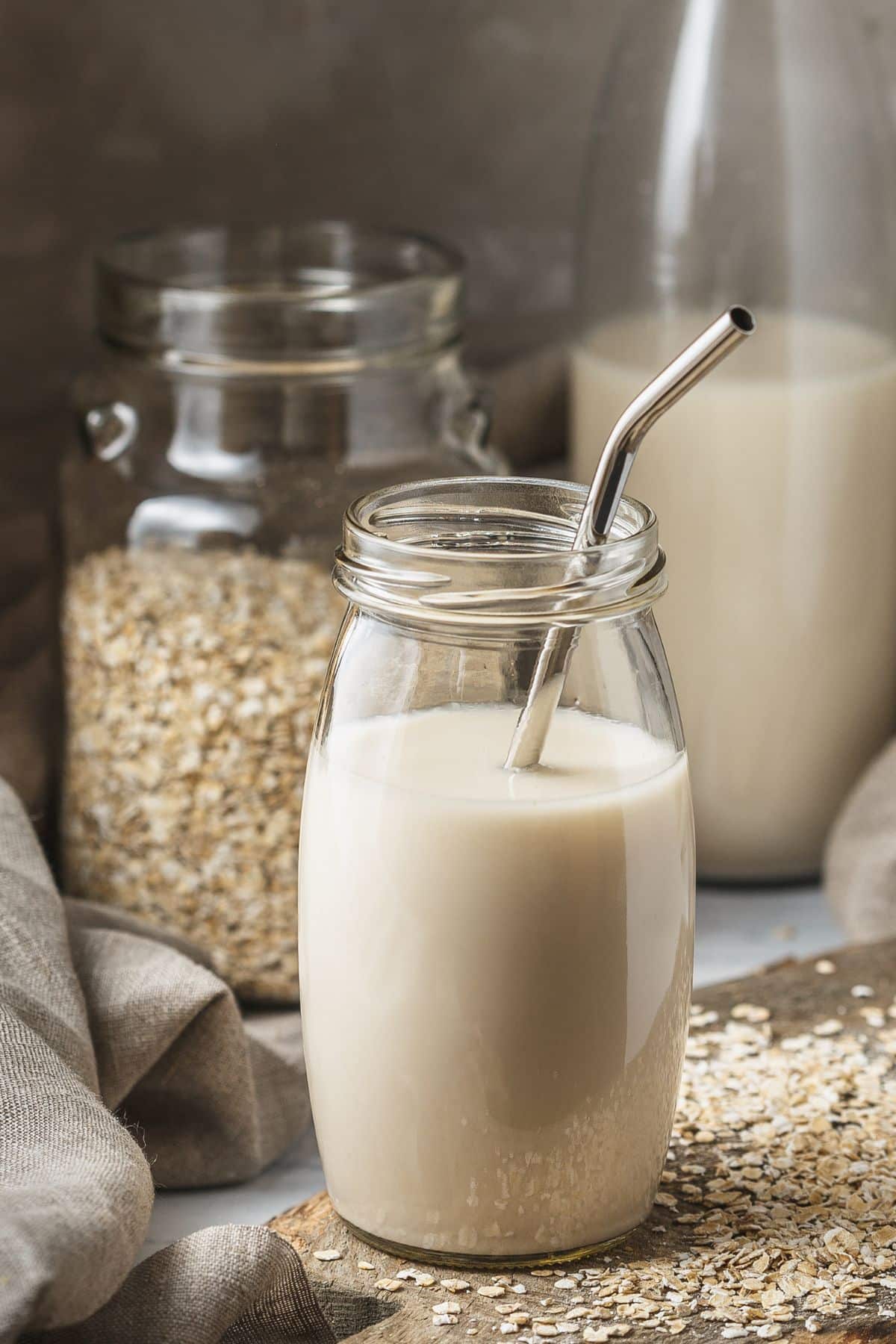 A glass of oat milk next to a jar of oats.