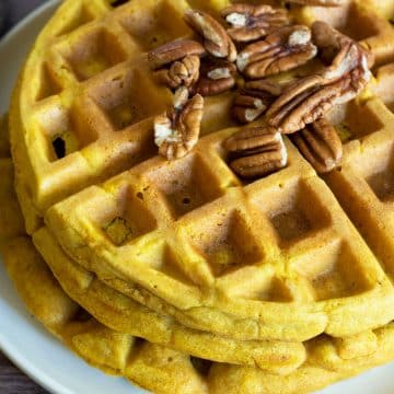 A stack of gluten free pumpkin waffles topped with pecans.