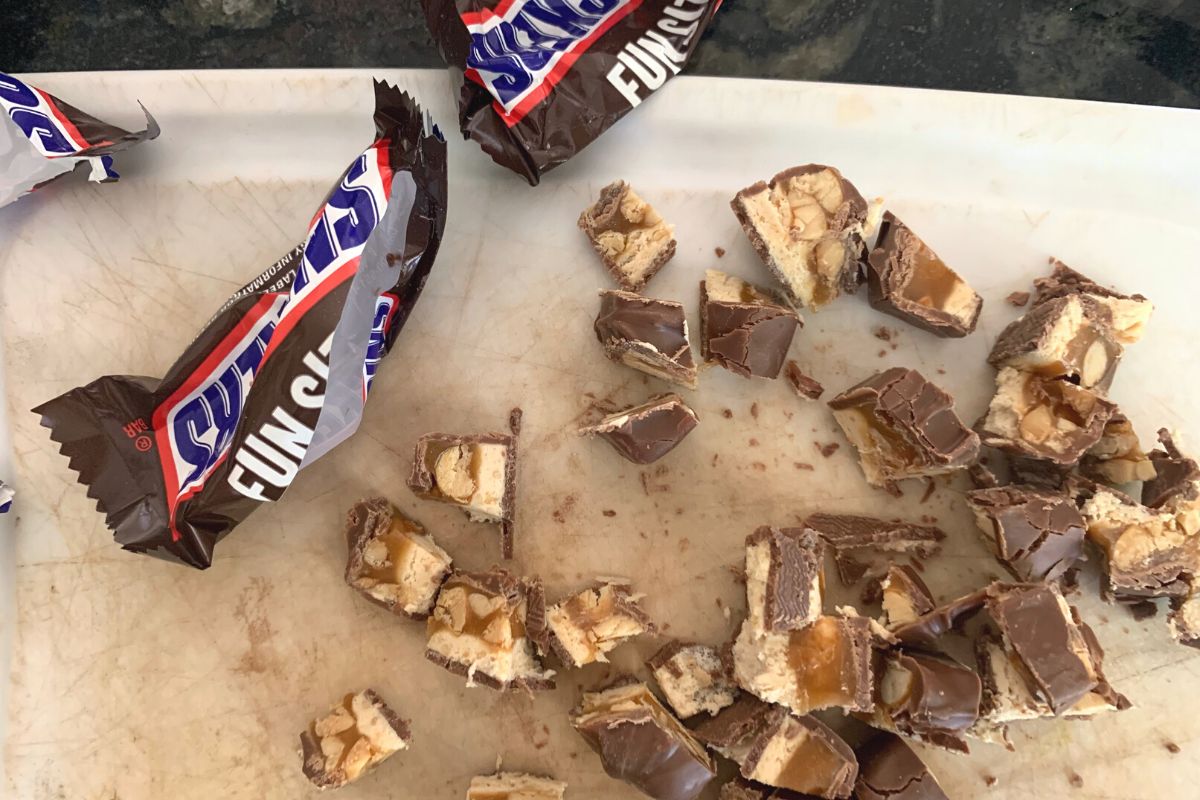 Chopped Snickers Fun Size Candy Bars on a cutting board.