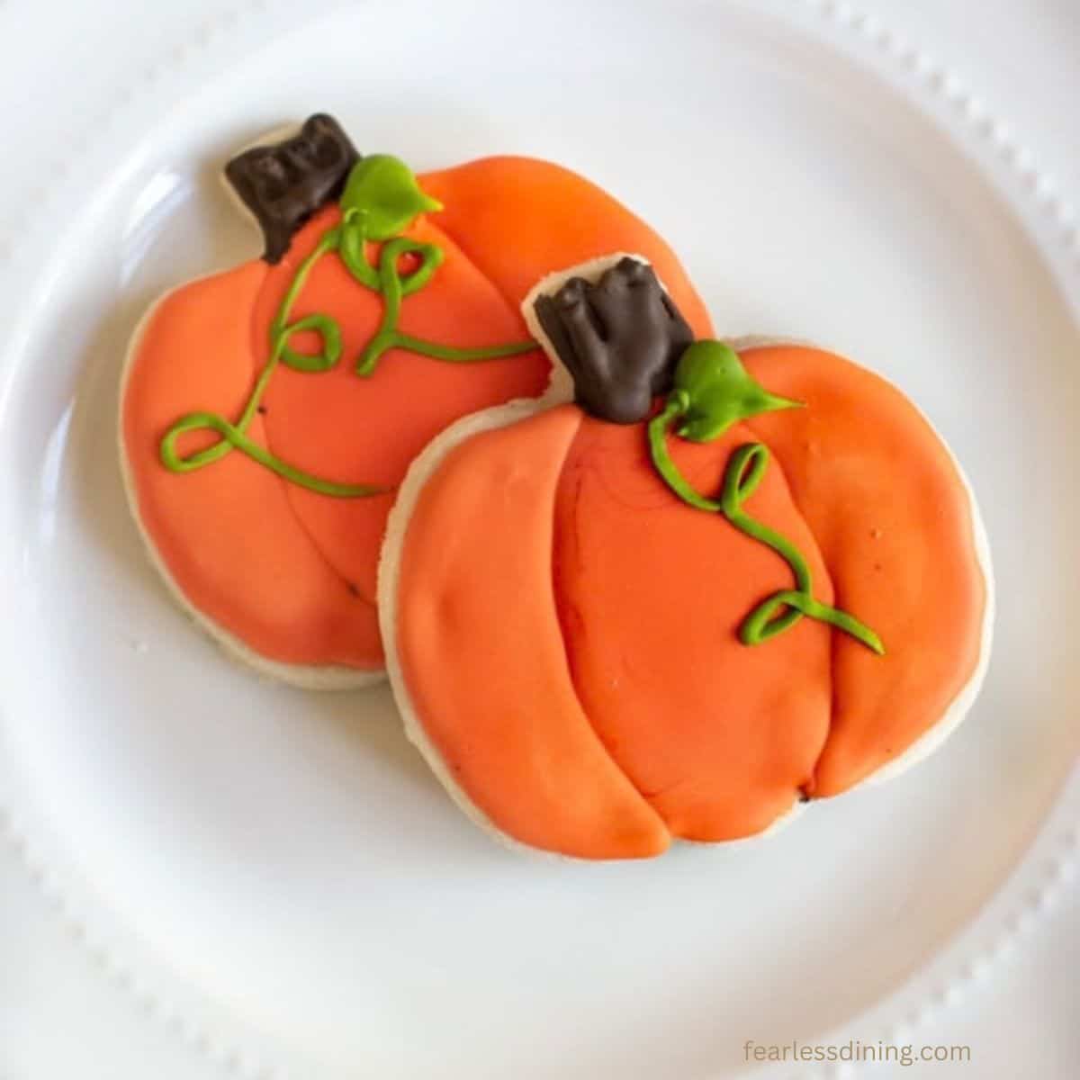 Two gluten free cut out cookies decorated with royal icing to look like pumpkins.