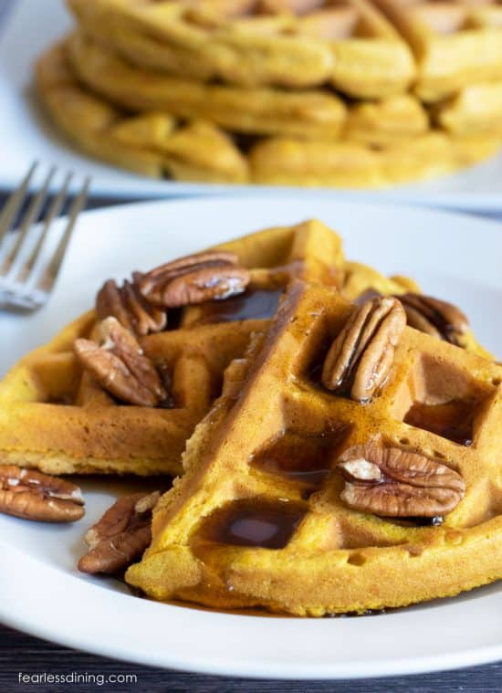 A plate of gluten-free pumpkin waffles with syrup and pecan halves.