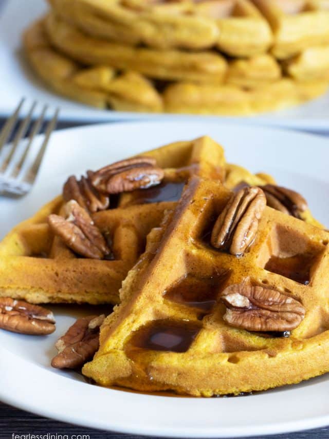 A plate of pumpkin waffles with syrup and pecan halves.